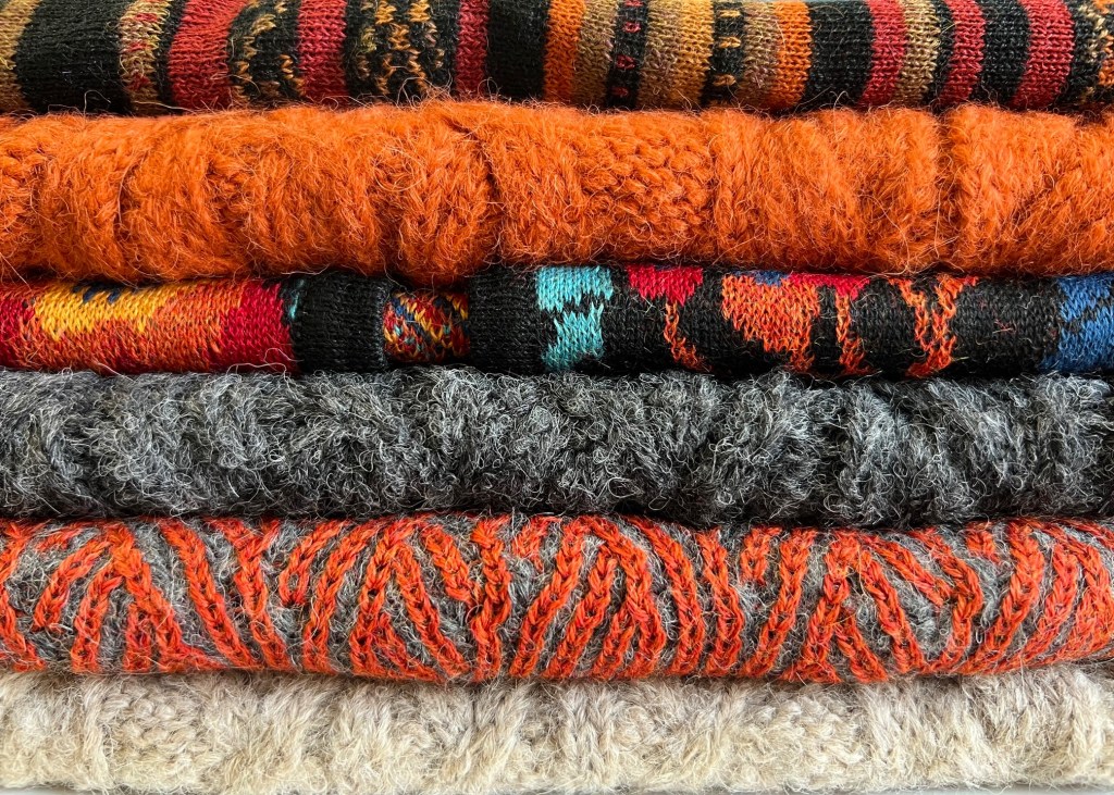 An image of colorful alpaca sweaters folded on top of each other